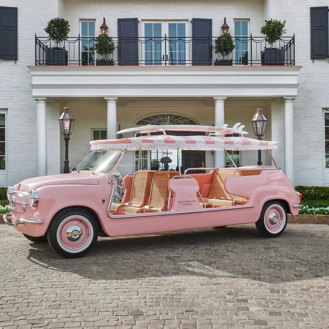 A pink car with seats in front of a white house.